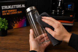 Microvezeldoek reinigt een glazen drinkfles voordat een UVDTF-transfer wordt aangebracht op een schone, vetvrije ondergrond.
